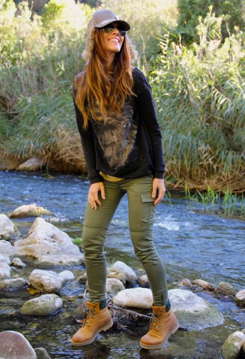 Chica parada en las piedras de un rió mientras usa un atuendo verde y botas timberland 