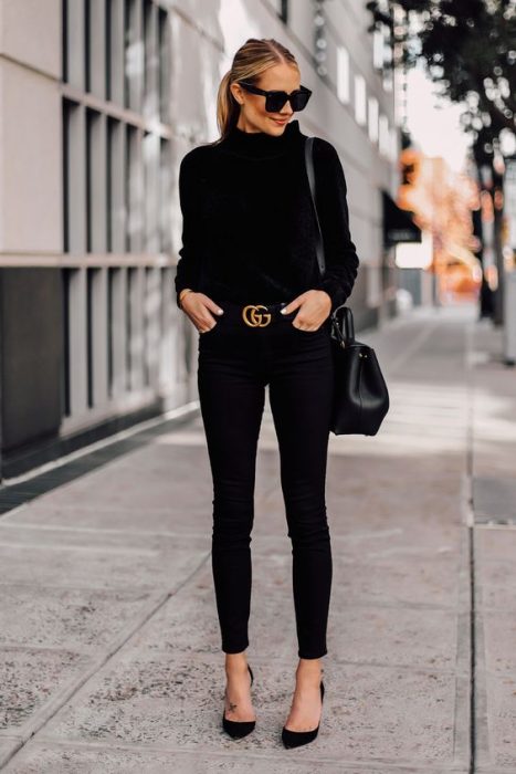 Chica por la calle luciendo un outfit negro en tacones y cinturón dorado