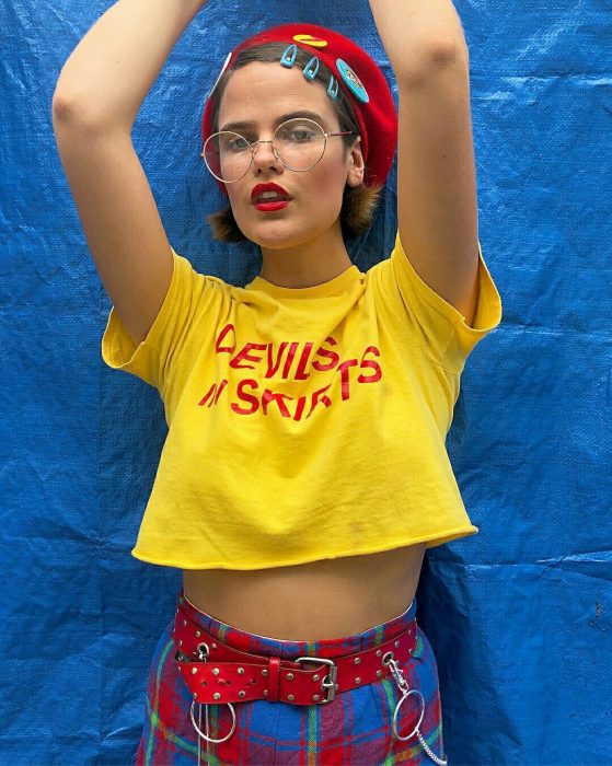 Chica luciendo una camiseta amarilla, pantalón de cuadros, un sombrero rojo y broches azules