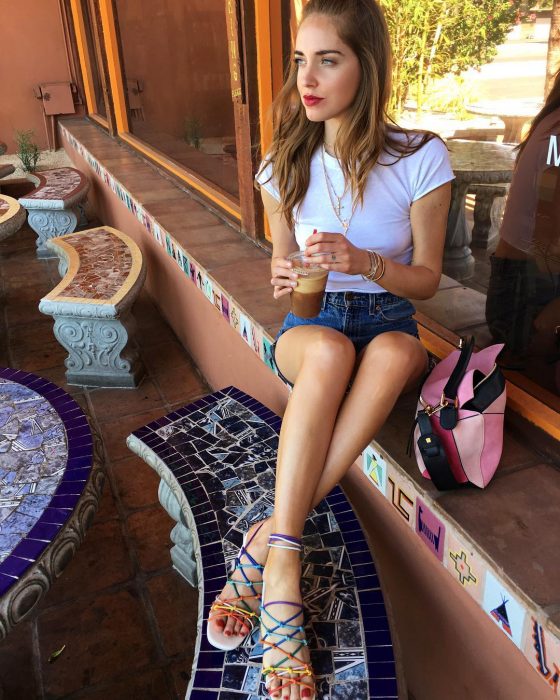 Chiara Ferragni sentada disfrutando de un café y mostrando su outfit, bolso rosa y sandalias de colores 