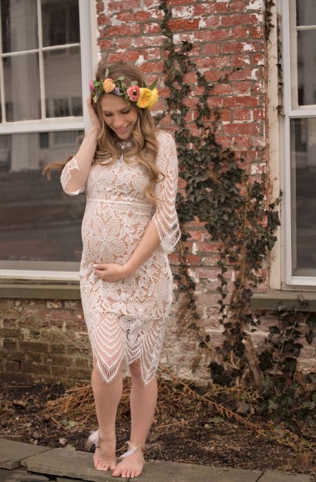 Vestido para baby shower, mujer embarazada con vestido corto de encaje color beige, descalza y con corona de flores en el cabello rubio
