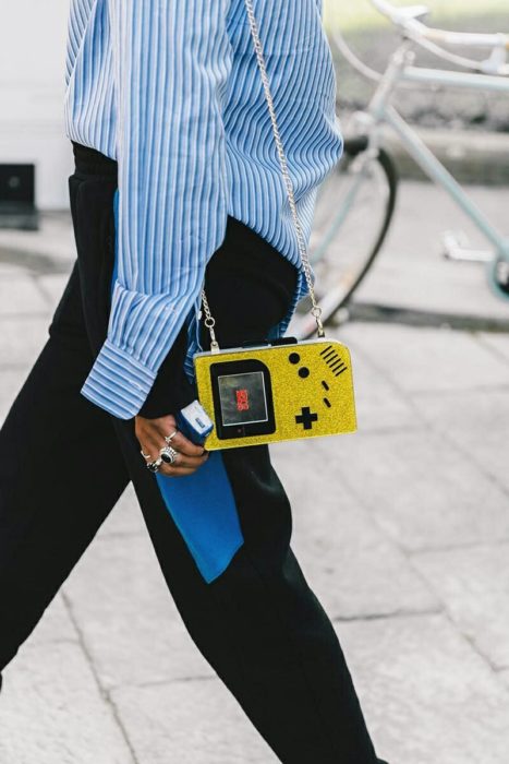 Chica caminando mientras sujeta una bolsa de color amarillo en forma de videojuego 