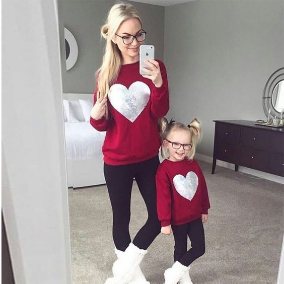 Madre e hija con outfits similares en sudadera roja decorada con un corazón y un pantalón oscuro