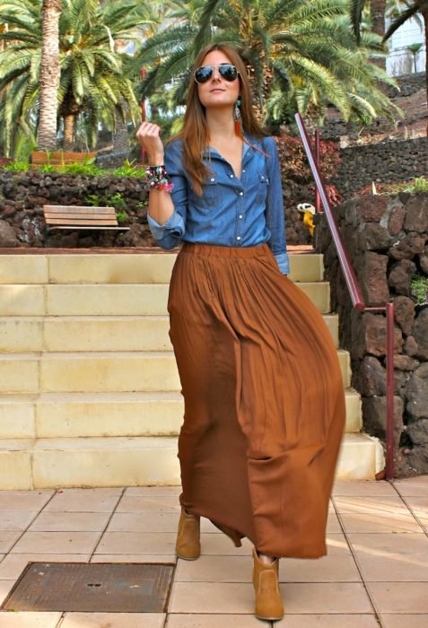 Chica usando una falda de color café, blusa de color azul mezclilla y botines de color café 