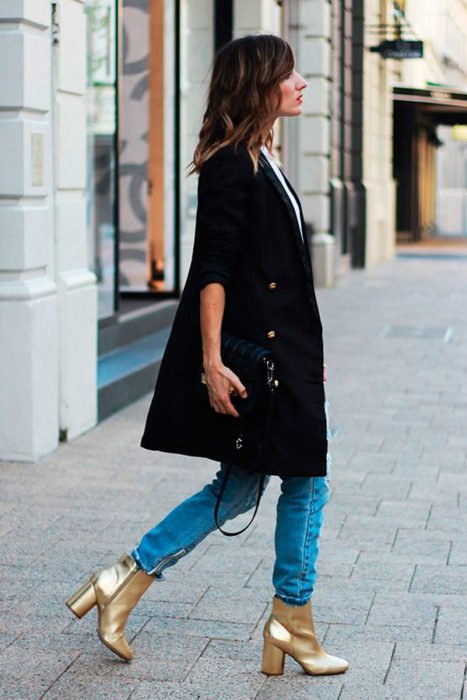 Chica caminando por la calle mientras usa unos botines de color dorado 