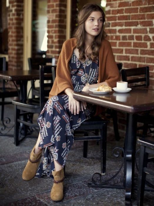 Ropa estilo boho o hippie chic; chica sentada en una mesa de un café con maxivestido holgado azul, con chal y botines