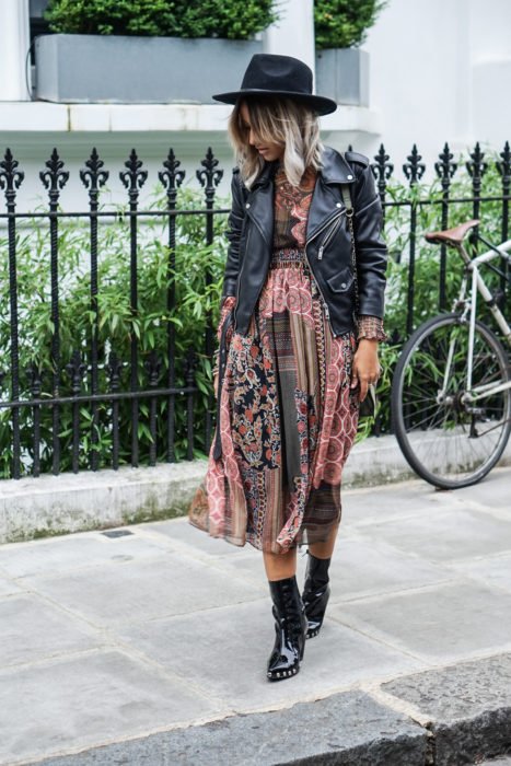 Ropa estilo boho o hippie chic; chica caminando en la calle, con vestido fresco de tela de paliacate, sombrero, chaqueta de piel negra y botines de charol