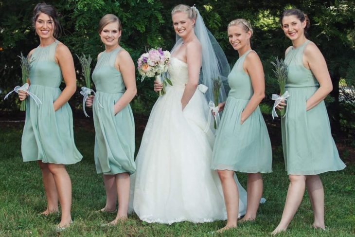 una novia y sus damas posan en un jardín, todas con la mano izquierda dentro del bolsillo de sus respectivos vestidos