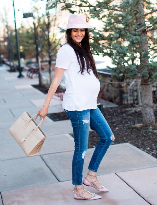 Chica embarazada usando una camisa blanca y jeans con sombrero 