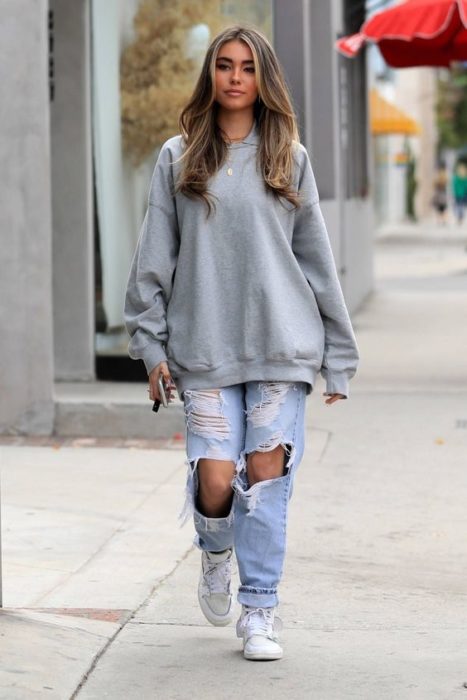 Chica llevando sudadera amplia en tono gris con jeans rotos