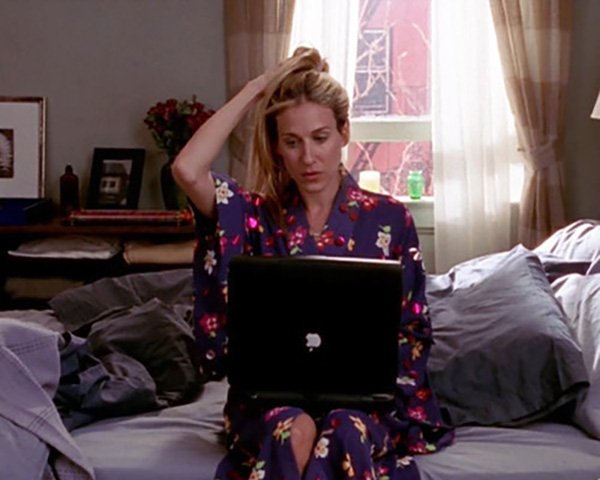 Carrie Bradshaw sentada en la cama con un kimono de flores morado