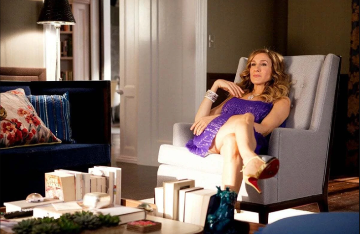 Carrie Bradshaw sentada en el sofá con vestido morado
