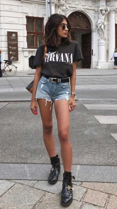 Chica con blusa de nirvana color negra y short de mezclilla con cinto y botas engras